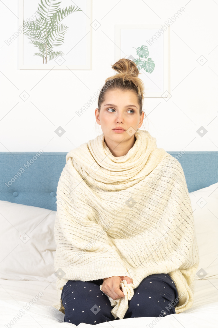 Front view of a young lady wrapped in white blanket sitting in bed