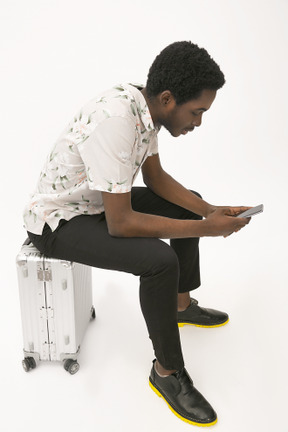 Afroman sitting on the baggage and using his smartphone