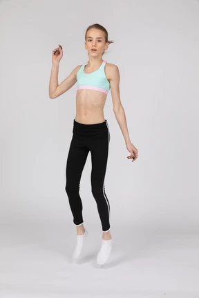 Three-quarter view of a teen girl in sportswear raising hand while jumping