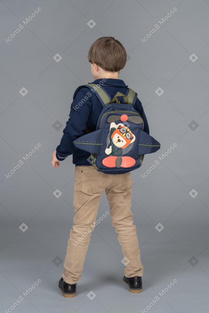 Little boy with a backpack standing with his back to camera
