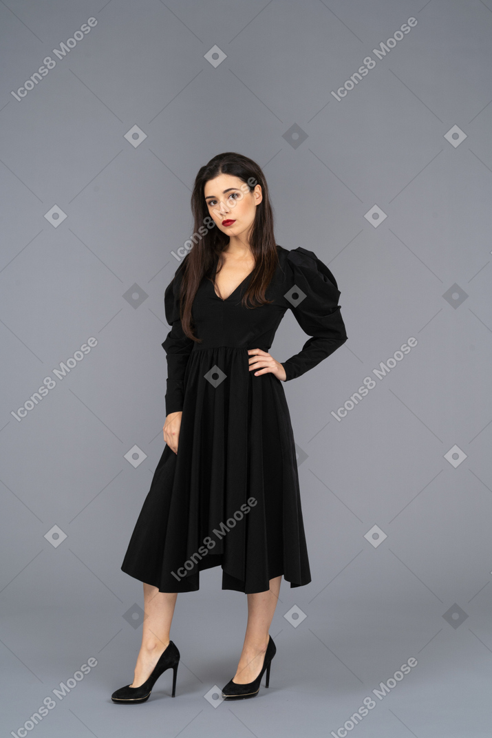 Vue de trois quarts d'une jeune femme dans une robe noire mettant la main sur la hanche