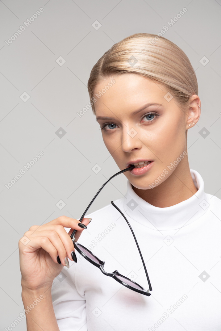 Donna attraente che tiene i suoi occhiali da sole vicino alla sua bocca nella posizione "premurosa"