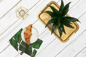 A plate with a croissant on it next to a potted plant