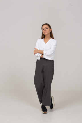 Vista frontale di una giovane donna prepotente in abiti da ufficio che cammina con le braccia incrociate