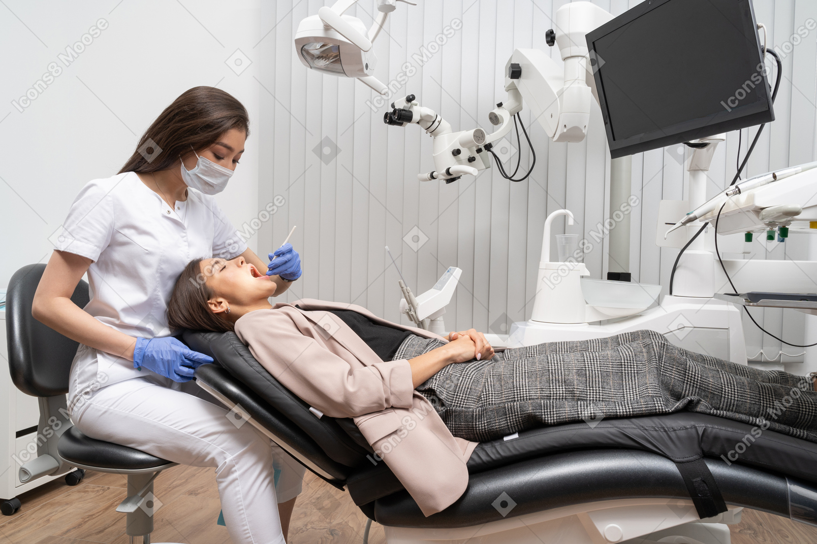 病院のキャビネットに横たわっている女性患者を診察する女性歯科医の全身像