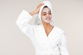 Black woman in white bathrobe and head towel enjoying her skin care routine