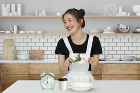 A smiling woman in an apron eating salad