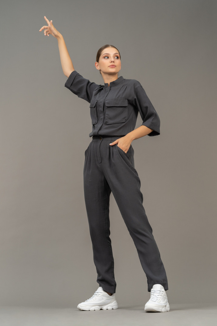 Front view of a young woman in a jumpsuit outstretching her arm
