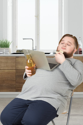 A man sitting in a chair with a laptop and a drink