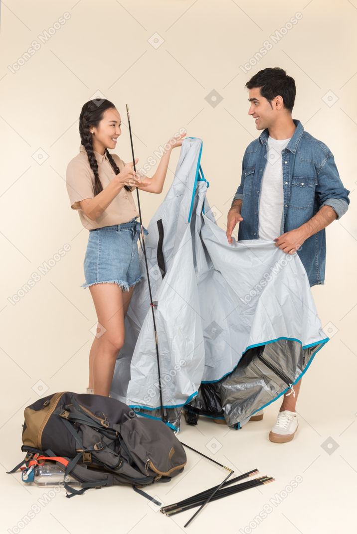 Laughing young interracial couple setting up a tent