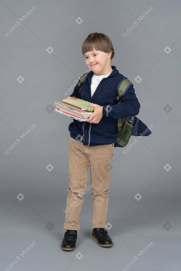 Fröhlicher kleiner junge mit einem rucksack, der bücher hält