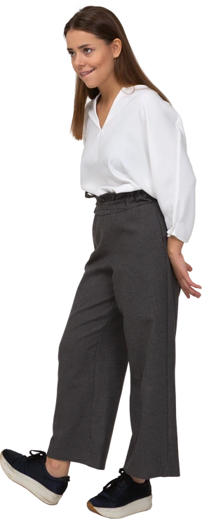 Three-quarter view of a sly young lady in office clothing holding hands behind