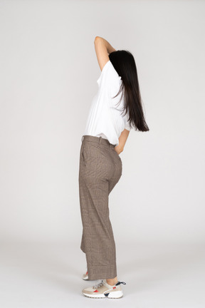 Three-quarter back view of a dancing young lady in breeches and t-shirt raising hands