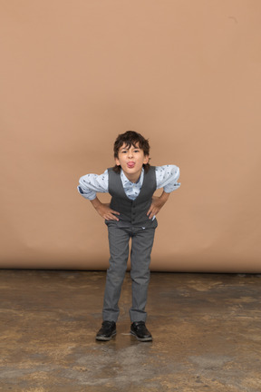 Vista frontal de un niño con traje de pie con las manos en las caderas y agachándose