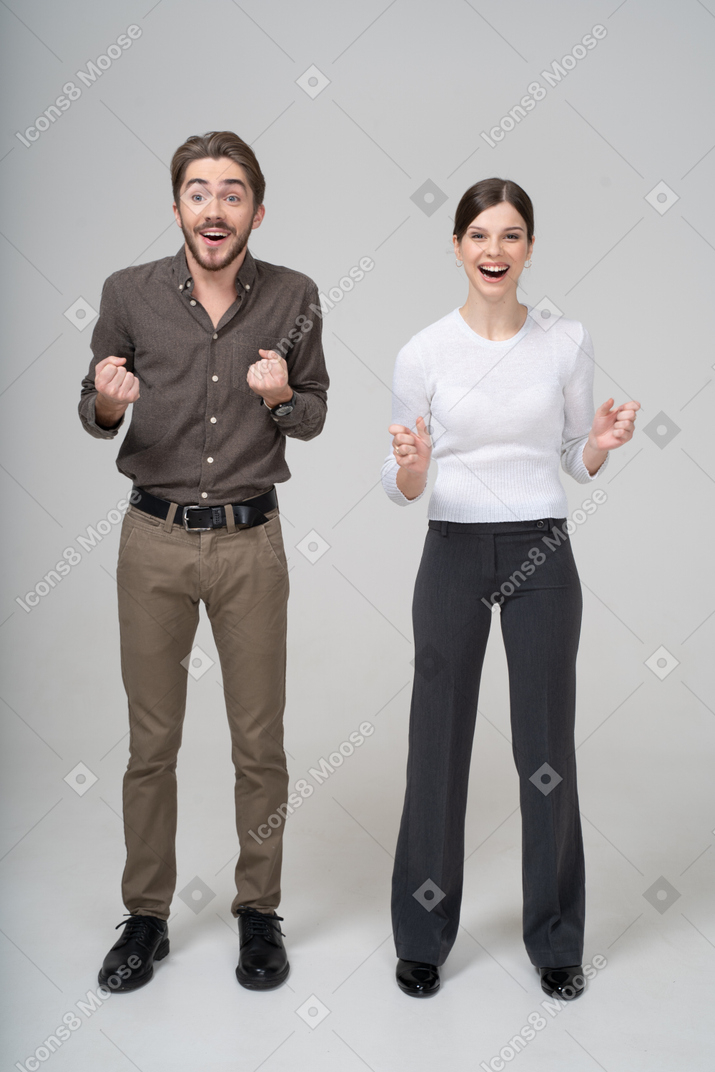 Vista frontal de um jovem casal encantado com roupas de escritório cerrando os punhos