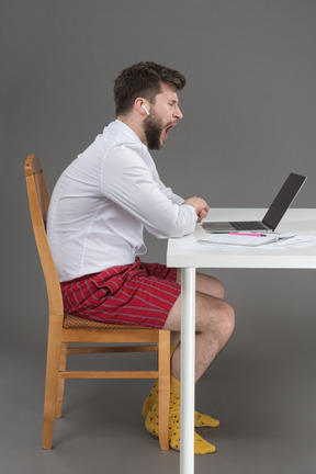 Trabajador soñoliento bostezando frente a una computadora portátil