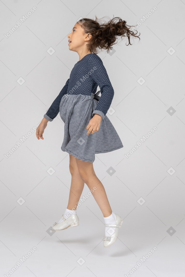 Vista lateral de una niña saltando alto en movimiento
