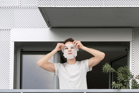 A man with a facial mask on standing on a balcony
