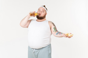 A fat man in sportswear drinking beer and sharing chips