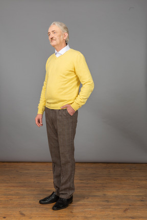 Dreiviertelansicht eines unzufriedenen alten mannes, der einen gelben pullover trägt und die hand in die tasche steckt und zur seite schaut