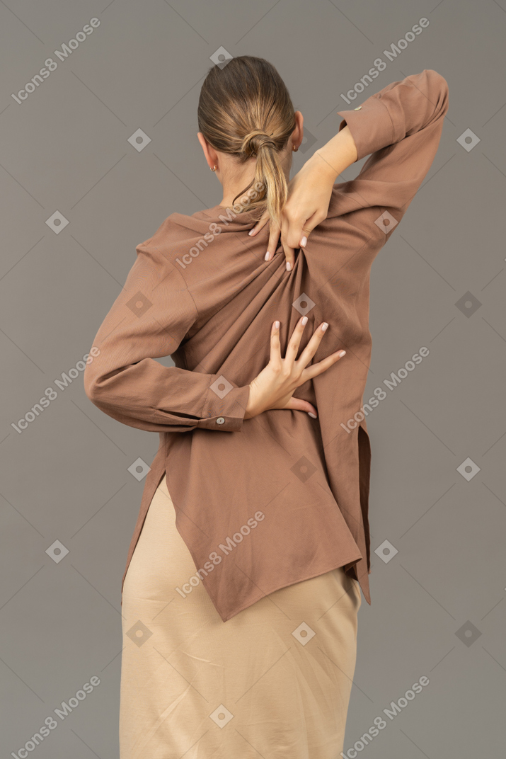 Back view of a woman reaching her back with a hand
