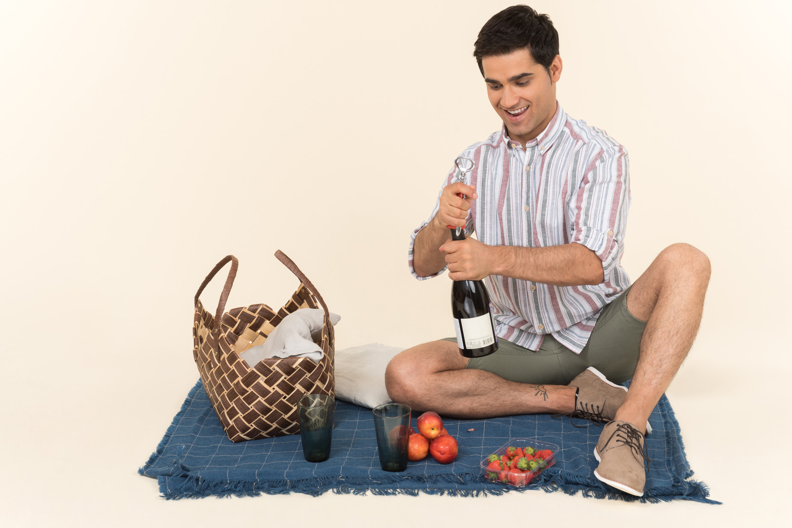 Young caucasian man sitting on the blanket and opening bottle of wine