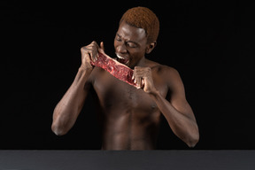 Front view of a young afro man biting a slice of meat