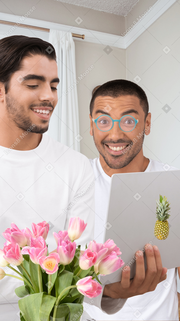 Two cheerful men with laptop and flowers in front of them