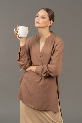 Giovane donna in possesso di una tazza di caffè che guarda da parte
