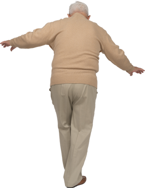 Vista trasera de un anciano con ropa informal caminando con los brazos extendidos