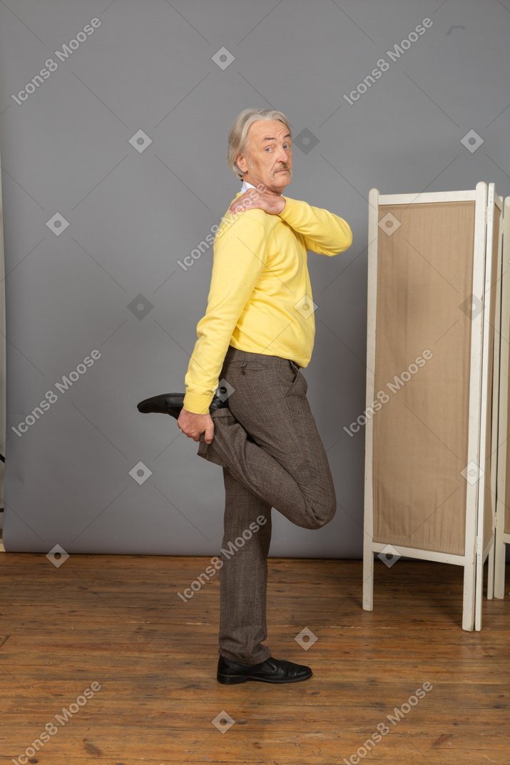 Side view of an old man holding his ankle while touching shoulder