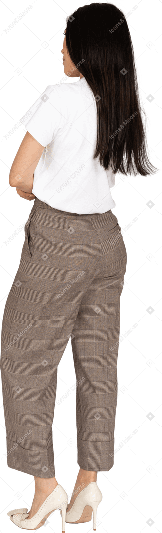 Vista posteriore di tre quarti di una giovane donna scontenta in calzoni e maglietta che incrocia le mani