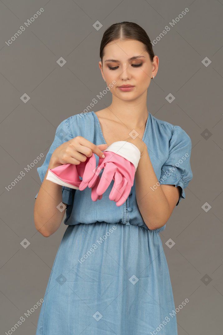 Young woman taking off pink latex gloves, looking bored