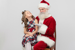 Criança menina sentada nos joelhos do papai noel