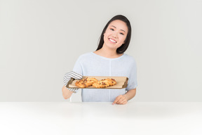 Sorridente jovem mulher asiática segurando a bandeja com cookies