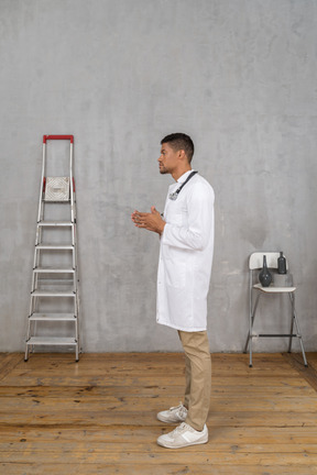 Вид сбоку на молодого врача, стоящего в комнате с лестницей и стулом, держась за руки вместе