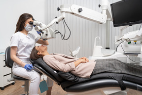 Pleine longueur d'une femme dentiste examinant sa patiente et regardant à travers le microscope