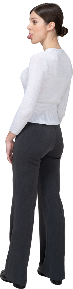 Vista posteriore di tre quarti di una giovane donna in abiti da ufficio che mostra la lingua