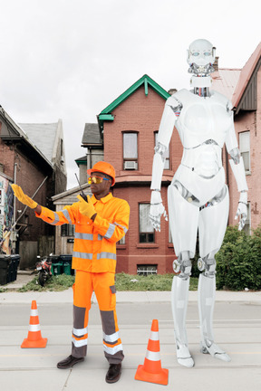 A man in an orange safety suit standing next to a robot