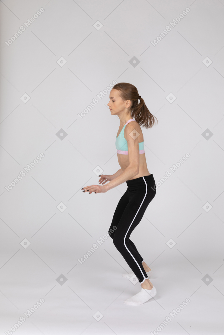 Side view of a teen girl in sportswear squatting and putting hands on hips