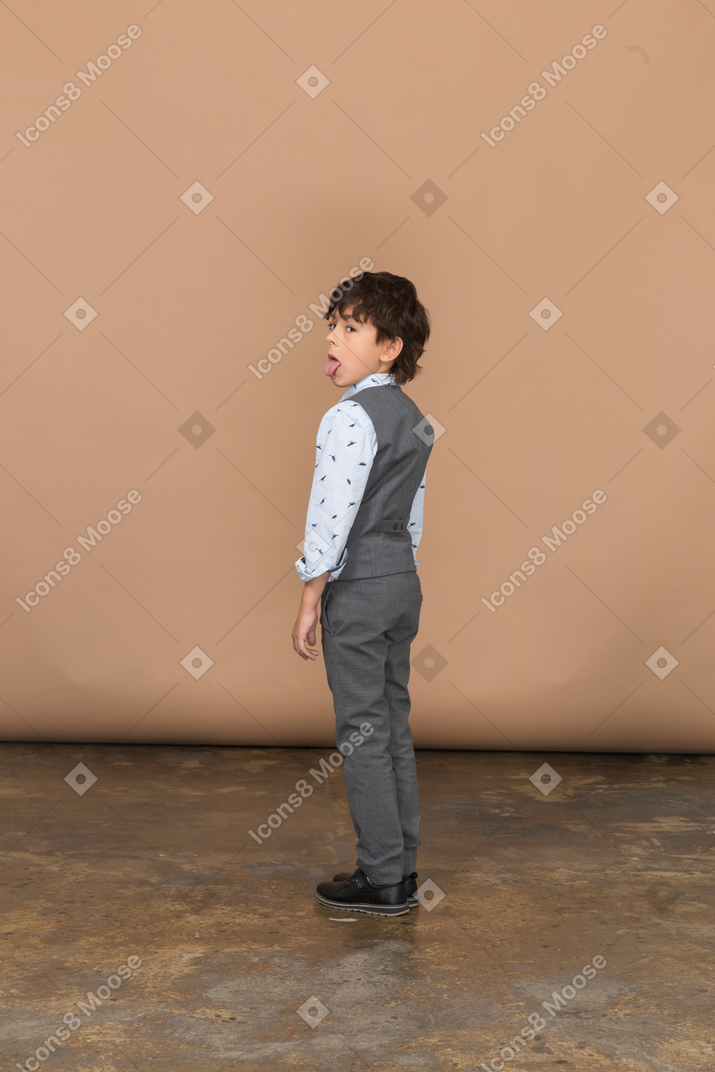 Vista lateral de um menino de terno cinza mostrando a língua