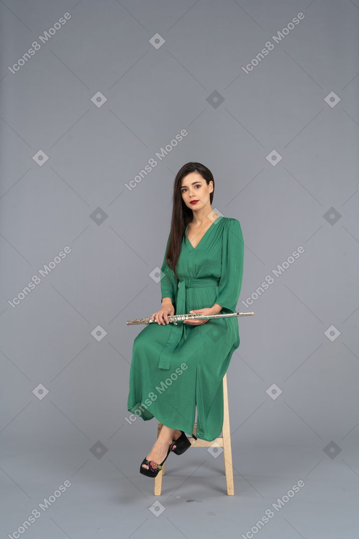 Three-quarter of a young lady in green dress sitting on a chair with a clarinet