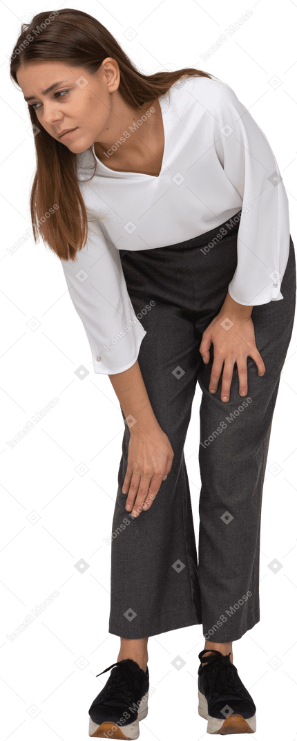 Vista frontal de una joven en ropa de oficina agacharse y tocar la rodilla