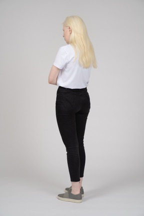 Vista posteriore di tre quarti di una giovane donna in piedi con le braccia conserte