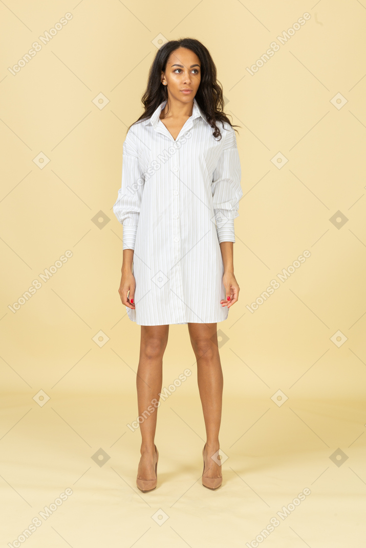 Vista frontal de una mujer joven de piel oscura confiada en vestido blanco mirando a un lado