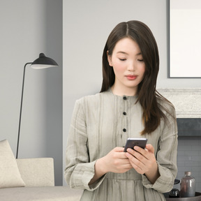 A woman standing in a living room looking at a cell phone