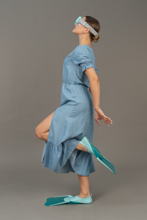 戴着浮潜面罩和脚蹼站在一条腿上的年轻女子的侧视图