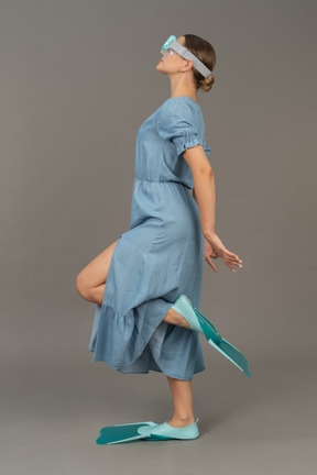 Side view of young woman standing on one leg in snorkelling mask and flippers