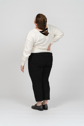 Rear view of plump woman in white sweater suffering from pain in lower back