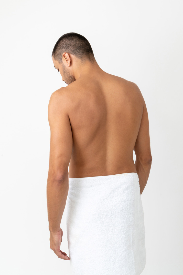 Wraped in towel barechested young man standing back t the camera